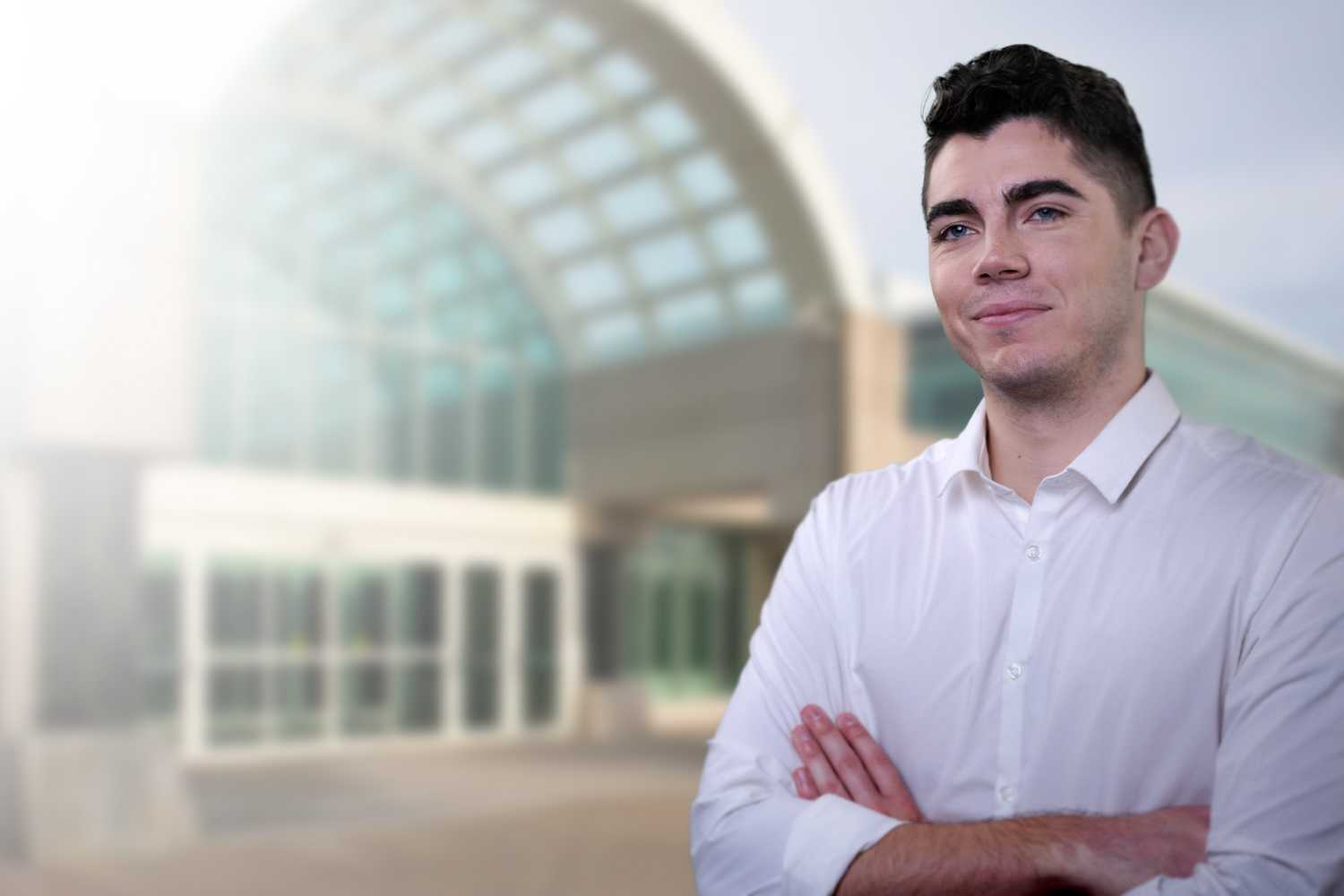 A man with light skin and short, dark hair standing in front of the entrance to CIA headquarters.